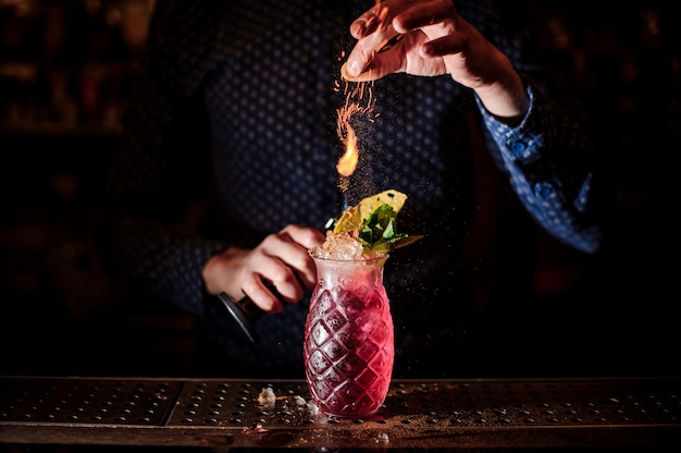 Barman aggiungendo spezie al cocktail estivo mojito alla fragola fresca e dolce con una nota di fumo