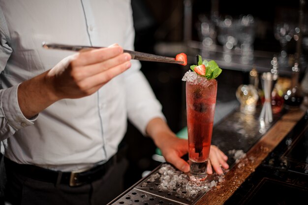 Barman che aggiunge una fragola al cocktail rosso trasparente fresco