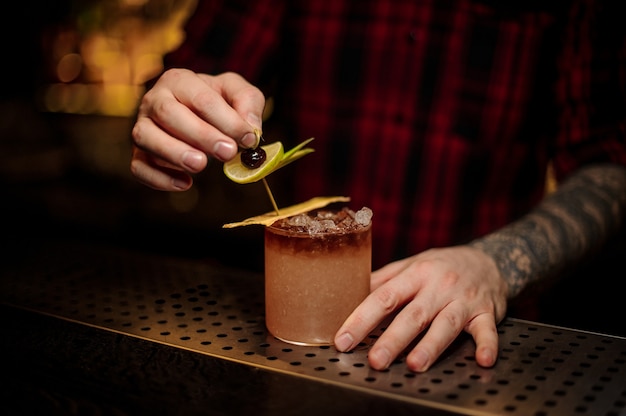 Barman che decora cocktail tropicale dolce e gustoso con fette di frutta sul bancone del bar