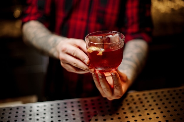 Barman che tiene una bevanda alcolica forte con whisky e scorza d'arancia sul bancone del bar