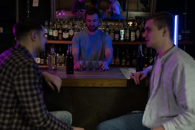 Barman che versa lo spirito duro nei bicchieri per due amici maschi che si rilassano in un bar
