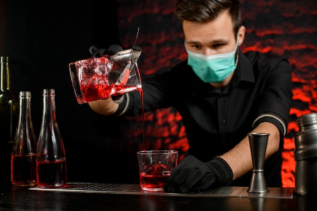 Barman con maschera versa magistralmente un cocktail freddo nel bicchiere