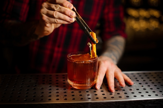 Barman decorare un bicchiere di cocktail con whisky con buccia d'arancia fresca sul bancone del bar