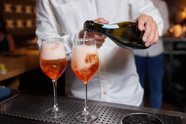 Barman in camicia e grembiule che fa una bevanda alcolica con il ghiaccio in un bicchiere da cocktail