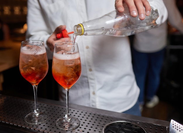 Barman in camicia e grembiule che fa una bevanda alcolica con il ghiaccio in un bicchiere da cocktail