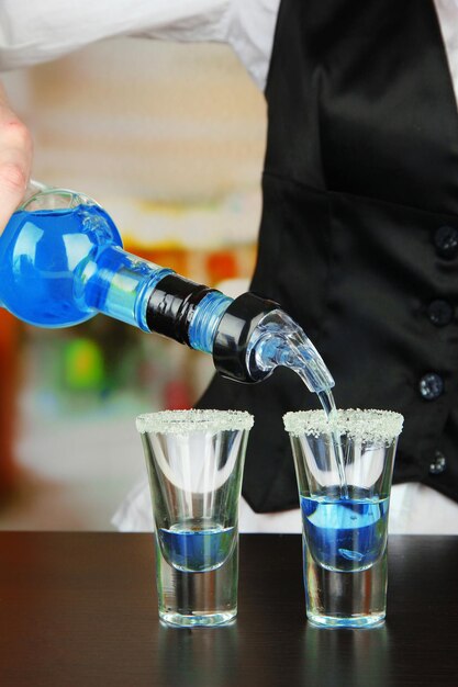 Barman mano con bottiglia versando bevande in bicchieri su sfondo luminoso