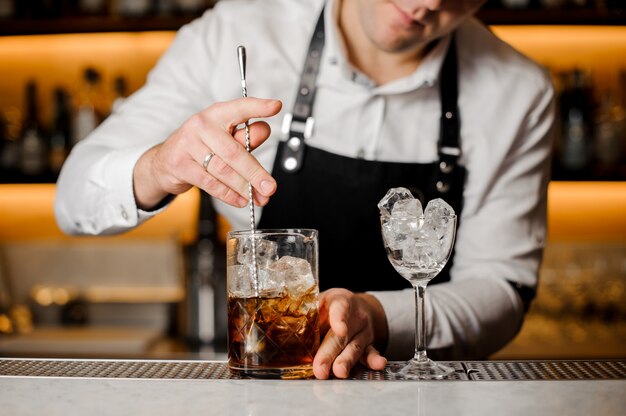 Barman mescolando cubetti di ghiaccio con bevanda alcolica