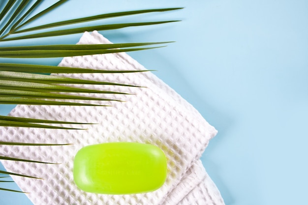 Barra di sapone verde sul piatto di sapone wppden e asciugamano da bagno, sfondo azzurro. Concetto di zero rifiuti eco friendly set da bagno. Vista dall'alto. Copia spazio.