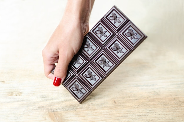 Barretta di cioccolato in una mano femminile con una manicure brillante.