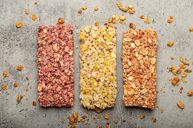 Barrette di cereali assortite con noci, semi, frutta e bacche su sfondo di pietra grigia, snack veloci e salutari o barrette di cereali dolci ricche di energia e fibre