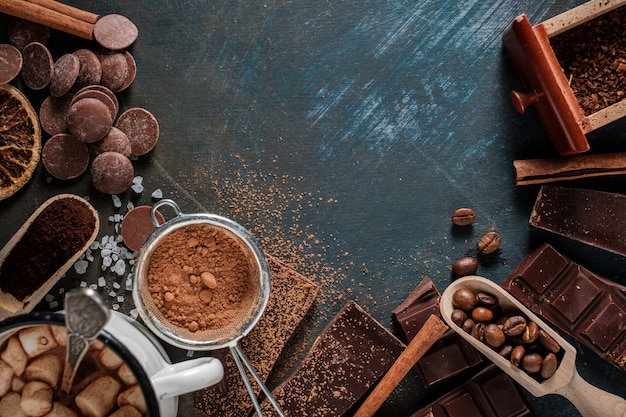 Barrette di cioccolato fondente e al latte con fettine di arancia secche, bastoncini di cannella e chicchi di caffè sulla superficie blu,