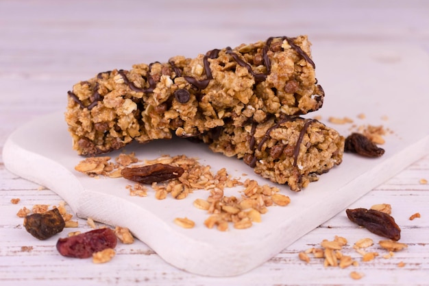 Barrette di muesli con noci e uvetta e pezzi di cioccolato su una tavola di legno bianca