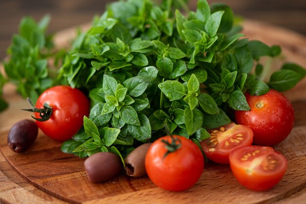 Basilico fresco con pomodori e olive su una tavola di legno