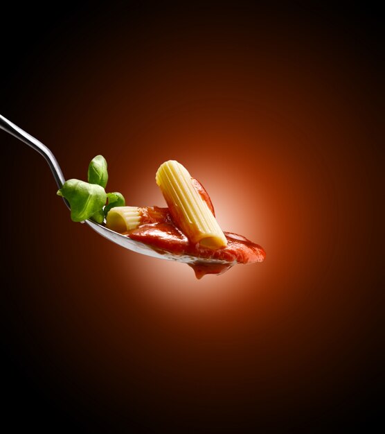 basilico vicino a pasta e salsa di pomodoro in un cucchiaio