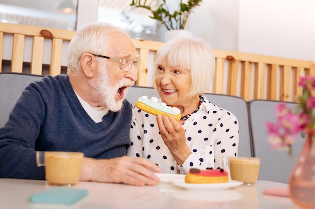 Basso angolo di donna senior attraente che tiene eclair e bocca di apertura dell'uomo maggiore