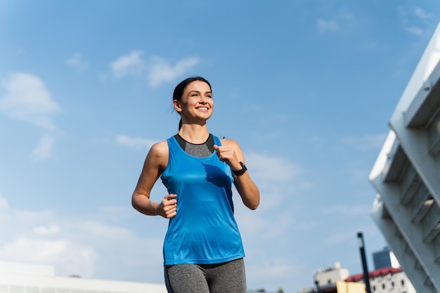 Basso angolo di sorridente donna allegra che fa jogging godendo il suo allenamento mattutino all'aperto