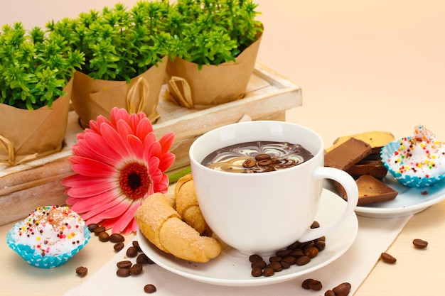 Bastoncini di cannella della tazza di caffè e dei fagioli della gerbera sulla tavola di legno