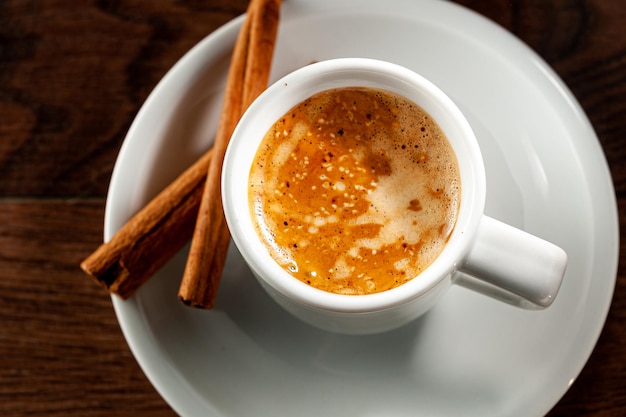 Bastoncini di cannella ed espresso in un bicchiere corto su fondo di legno