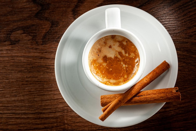 Bastoncini di cannella ed espresso in un bicchiere corto su fondo di legno