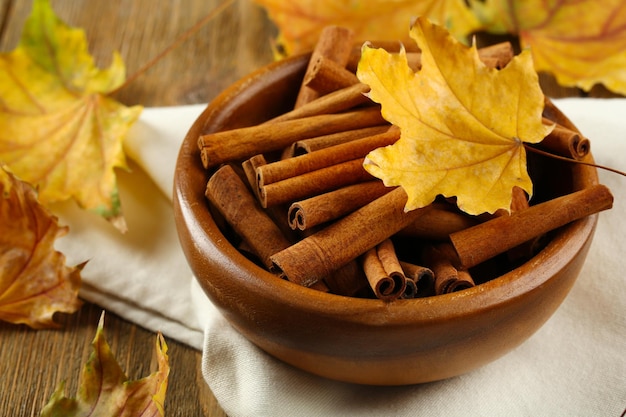 Bastoncini di cannella in una ciotola con foglie gialle su fondo di legno