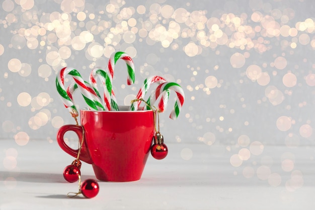 Bastoncini di caramelle di Natale in una tazza di caffè rossa con decorazione di ornamenti