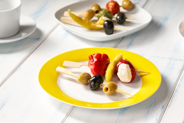 Bastoncini di finger food con olive e peperoni ripieni su piatto giallo.