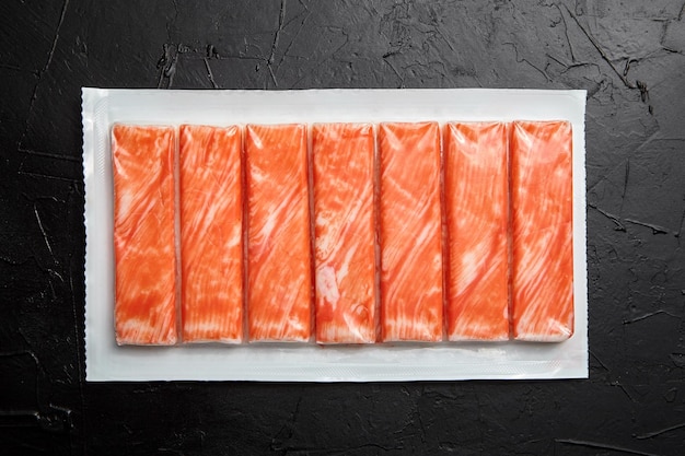 Bastoncini di granchio o surimi di carne di granchio imitazione in un pacchetto su vista da tavolo nera