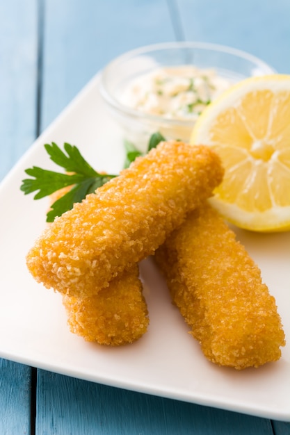 Bastoncini di pesce fritti croccanti con il limone e la salsa su legno blu