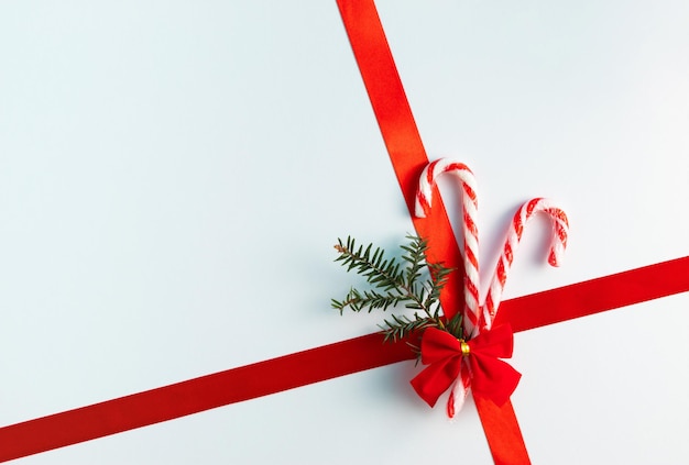 Bastoncini di zucchero di Natale con nastro rosso e abete su sfondo bianco Concetto di regalo di vacanza minimo Spazio per la copia piatta
