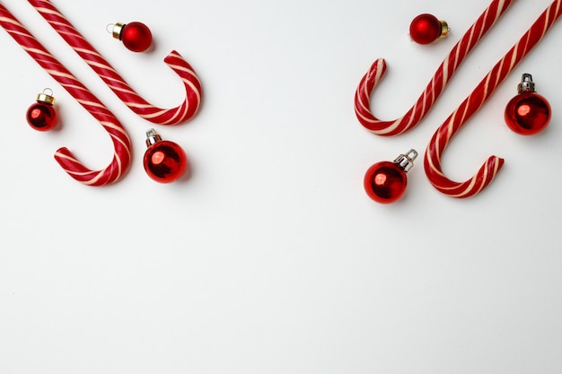 Bastoncini di zucchero e palline di Natale rosse su bianco piatto laico, vista dall'alto