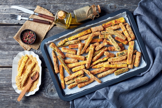 Bastoncini di zucchine croccanti impanati con pangrattato panko, parmigiano, spezie su una teglia, spuntino estivo sano, vista orizzontale dall'alto, piatto lay