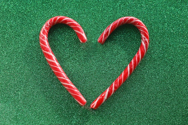 Bastoncino di zucchero natalizio a strisce di Babbo Natale a forma di cuore su sfondo verde rosso Simbolo dell'amore del nuovo anno