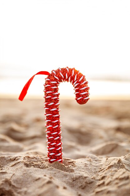 Bastoncino di zucchero rosso di Natale festivo sulla spiaggia sabbiosa al tramonto