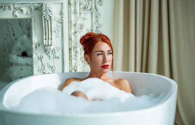 Bath girl foam I capelli rossi della giovane donna allegra sono sdraiati nella vasca da bagno con relax Concetto di purezza e comfort Bella ragazza dai capelli rossi prende il bagnoschiuma Bella donna in bagno