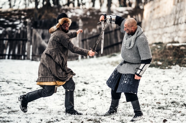 Battaglia di due guerrieri in armatura con armi che combattono con le spade nella neve