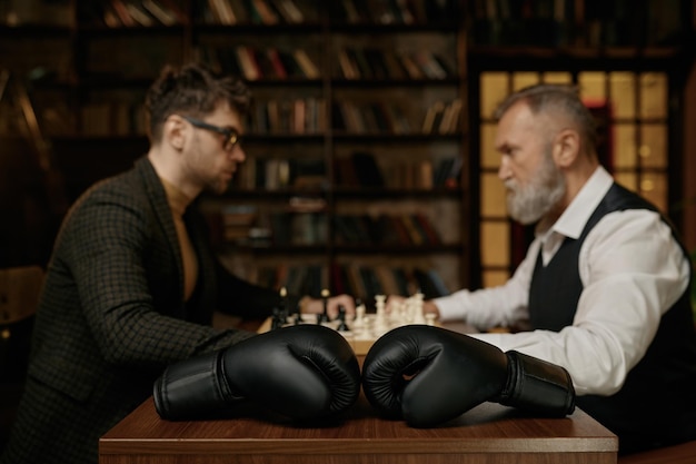 Battaglia di scacchi senior contro giovane uomo adulto con attenzione selettiva sui guanti boxer. Idee imprenditoriali, concorrenza e concetto di sfida strategica