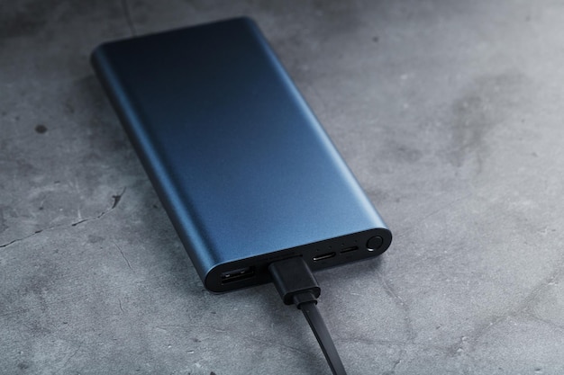 Batteria esterna portatile Power Bank blu con cavo USB su sfondo scuro strutturato per caricare i gadget