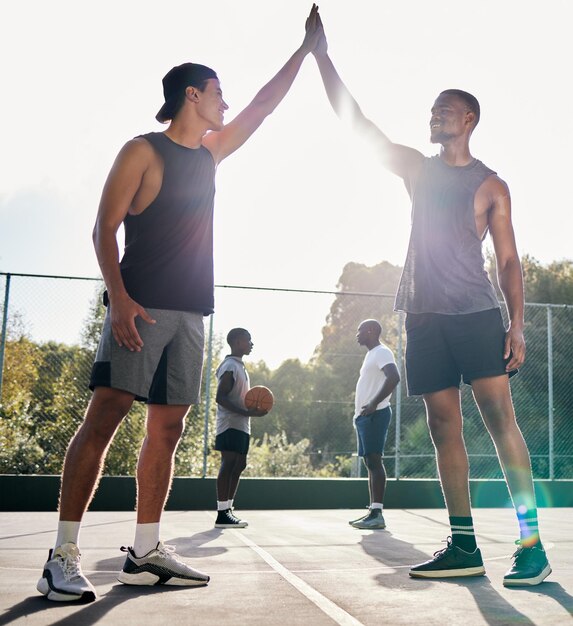 Batti il cinque nel basket e lavoro di squadra con un amico sportivo che festeggia come vincitore su un campo Obiettivo di fitness o successo con un giocatore di basket maschio e un amico che festeggia un risultato vincente