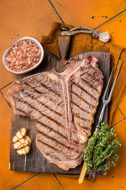 BBQ Roast T bone o carne di manzo Porterhouse Bistecca su una tavola di legno con spezie Sfondo arancione Vista dall'alto