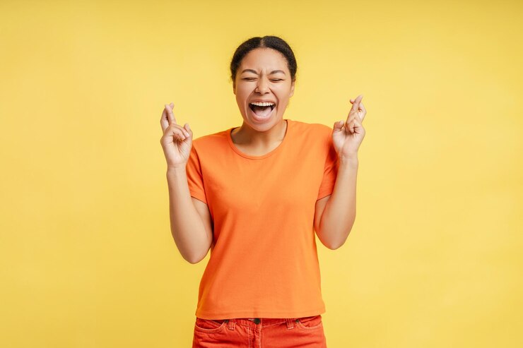 Photo beautiful stylish stunning african american woman wearing orange casual shirt closing her eyes and fingers crossed expressing positivity and hopefulness isolated over yellow background