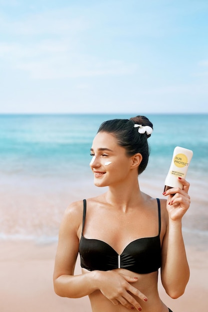 Beauty Woman Crema solare per la cura della pelle che tiene le bottiglie nelle sue mani Ragazza abbronzante che applica crema solare sul viso