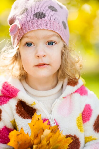 Bel bambino con foglie di acero gialle nel parco autunnale