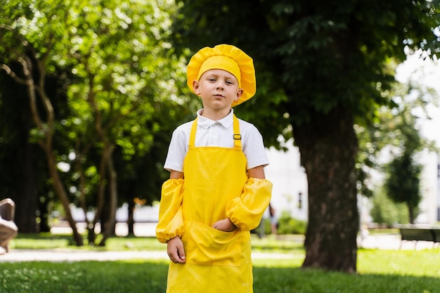 Bel bambino cuoco con cappello da chef giallo e grembiule uniforme gialla in posa all'aperto Pubblicità creativa per negozio di alimentari e bar