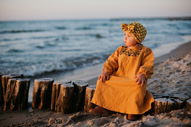 Bel bambino seduto sul frangiflutti sulla spiaggia del Mar Baltico all'ora dell'alba