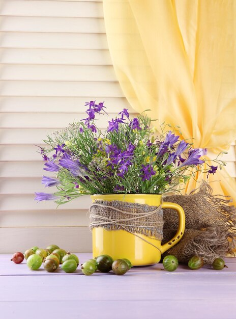 Bel bouquet di fiori di campo in tazza e frutti di bosco sulla tavola di legno
