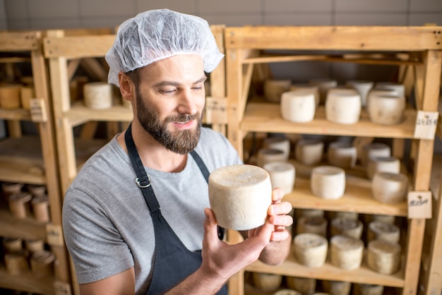 Bel casaro che controlla il processo di invecchiamento del formaggio di capra in piedi nella piccola cantina