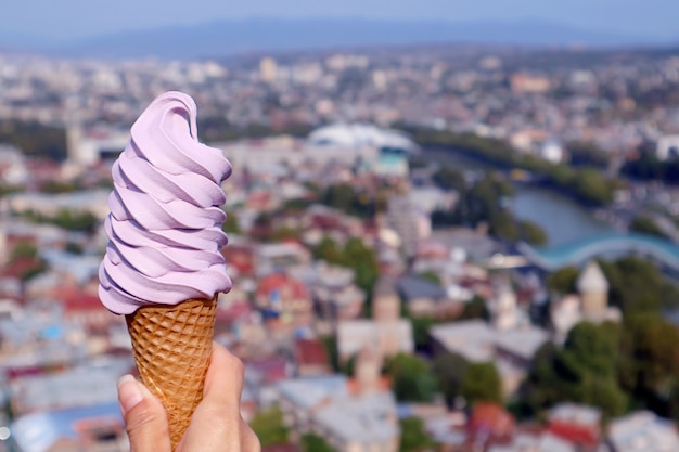 Bel colore lilla vino georgiano soft servire cono gelato in mano contro sfocata vista aerea della città di Tbilisi