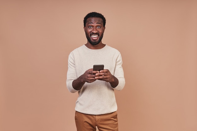 Bel giovane africano in abbigliamento casual utilizzando smart phone e sorridente
