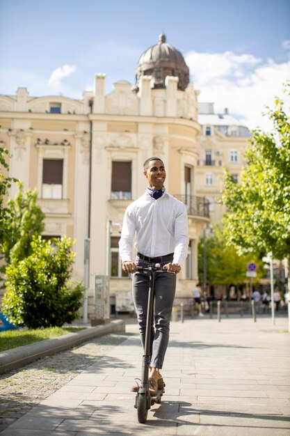 Bel giovane afroamericano utilizzando scooter elettrico su una strada