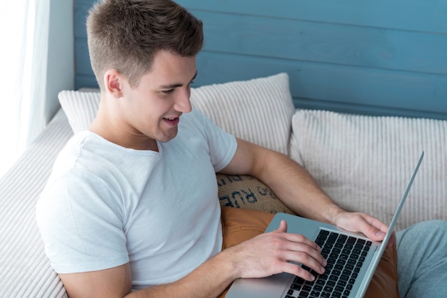 Bel giovane ambizione sorridente e utilizzando laptop mentre riposa sul divano